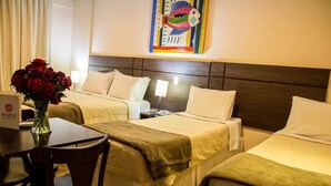 A hotel room with two beds, a desk with a vase of red roses, and a painting on the wall. - Hotel Maruá (São José dos Campos)