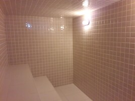 Un espacio de ducha con azulejos, suelo blanco y una lámpara en el techo.