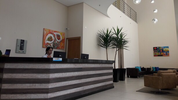 A reception area with a reception desk, a large potted plant, a staircase, and a colorful artwork on the wall. - Hotel Maruá (São José dos Campos)