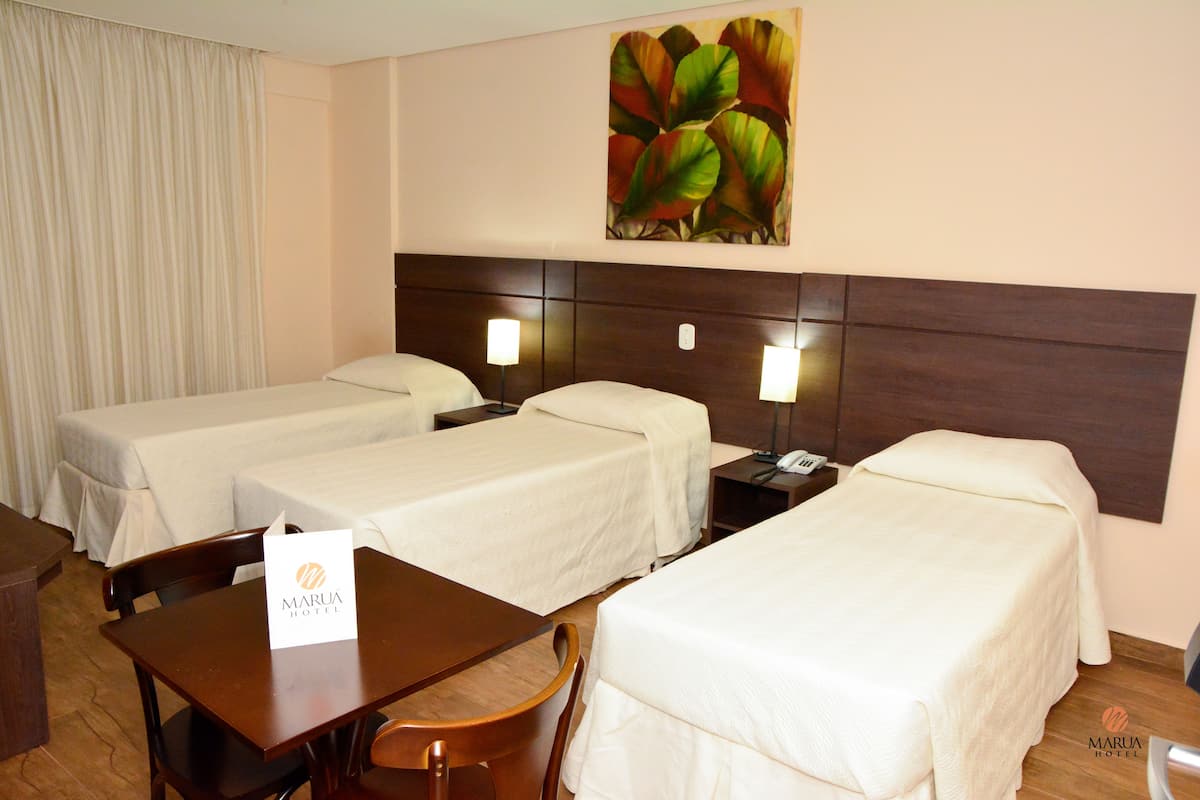 Ein Hotelzimmer mit drei Einzelbetten, einem Holztisch und einem Stuhl.