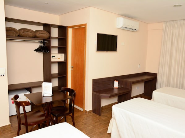 Habitación de hotel con escritorio, silla, dos camas, televisor y aire acondicionado.