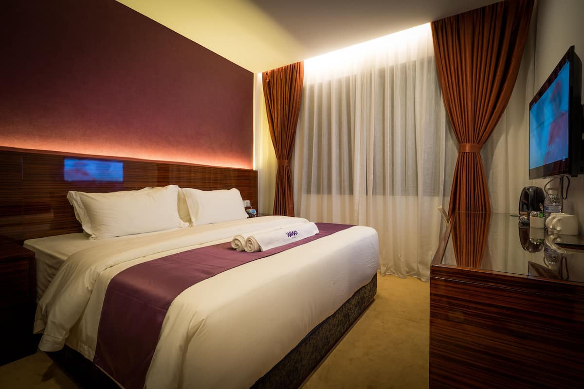 Une chambre d’hôtel avec un grand lit, une tête de lit en bois, un téléviseur à écran plat, un bureau avec un téléphone et un miroir.