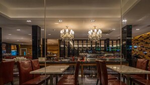 Un restaurante moderno con un separador de vidrio, sillas de madera y candelabros.