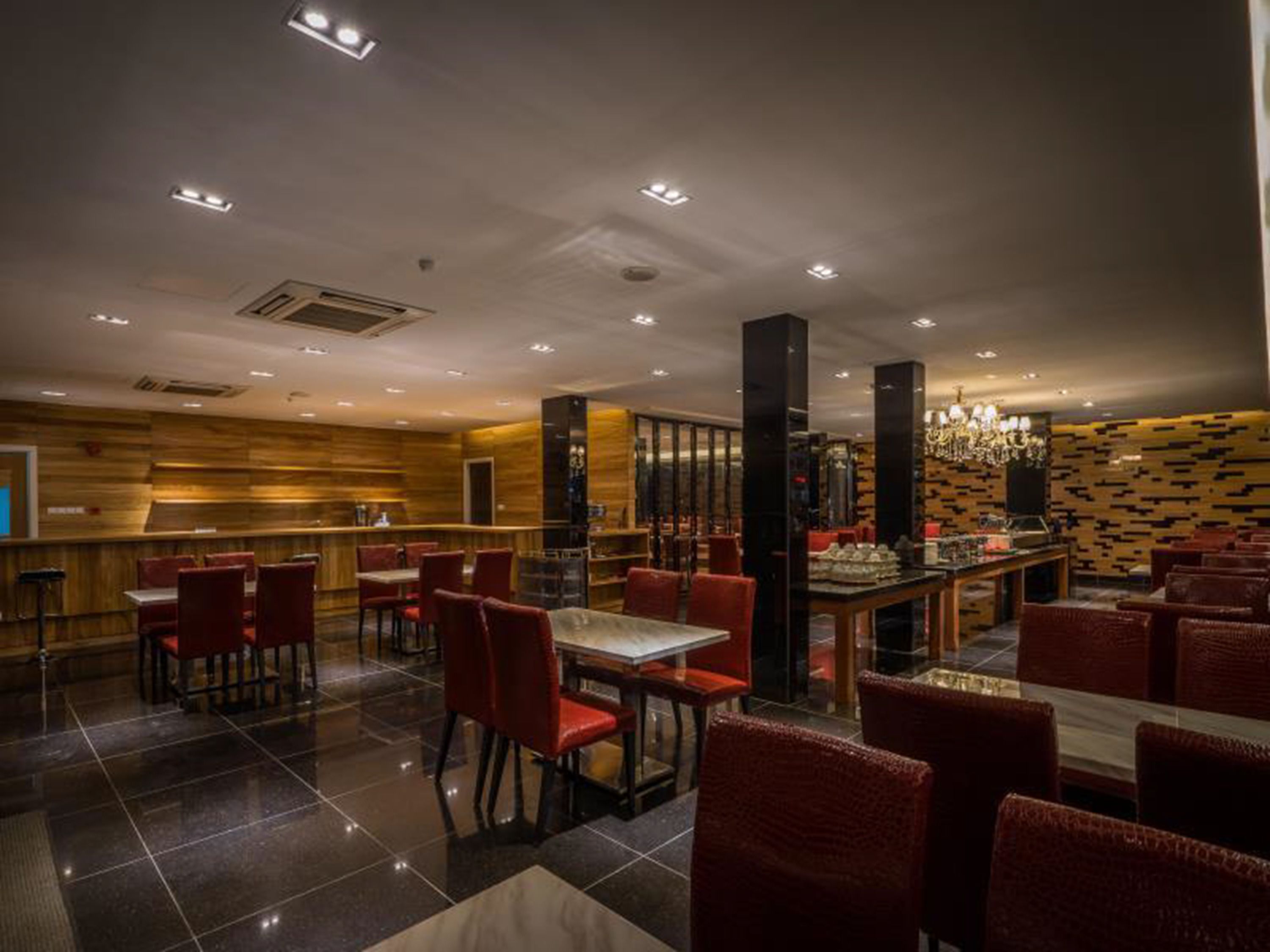 A restaurant with a modern interior, featuring red upholstered chairs, a bar area, and a patterned wall.