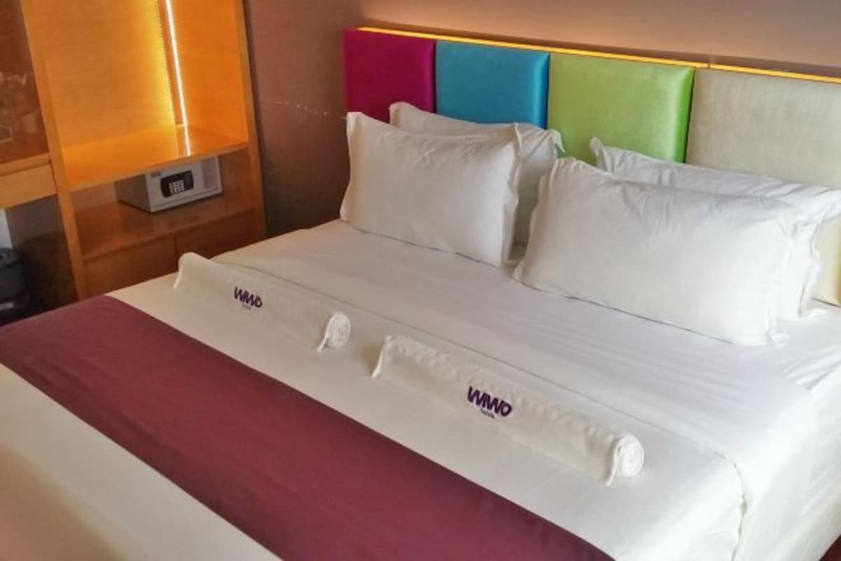 A hotel room with a bed, white bedding, a red blanket, and a headboard with colorful panels.