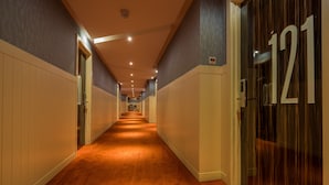 Un pasillo largo y estrecho con piso alfombrado, paneles de madera en las paredes y una puerta con el número 121.