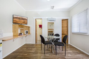 A compact kitchen with a microwave, a wooden shelf, and a glass table with four chairs. - Tamworth Lodge Motel (South Tamworth)