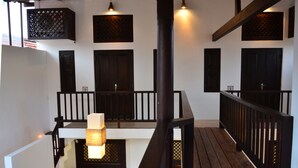A wooden balcony with a railing, a hanging light fixture, and a door with a number. - 56 by Deco (Galle)