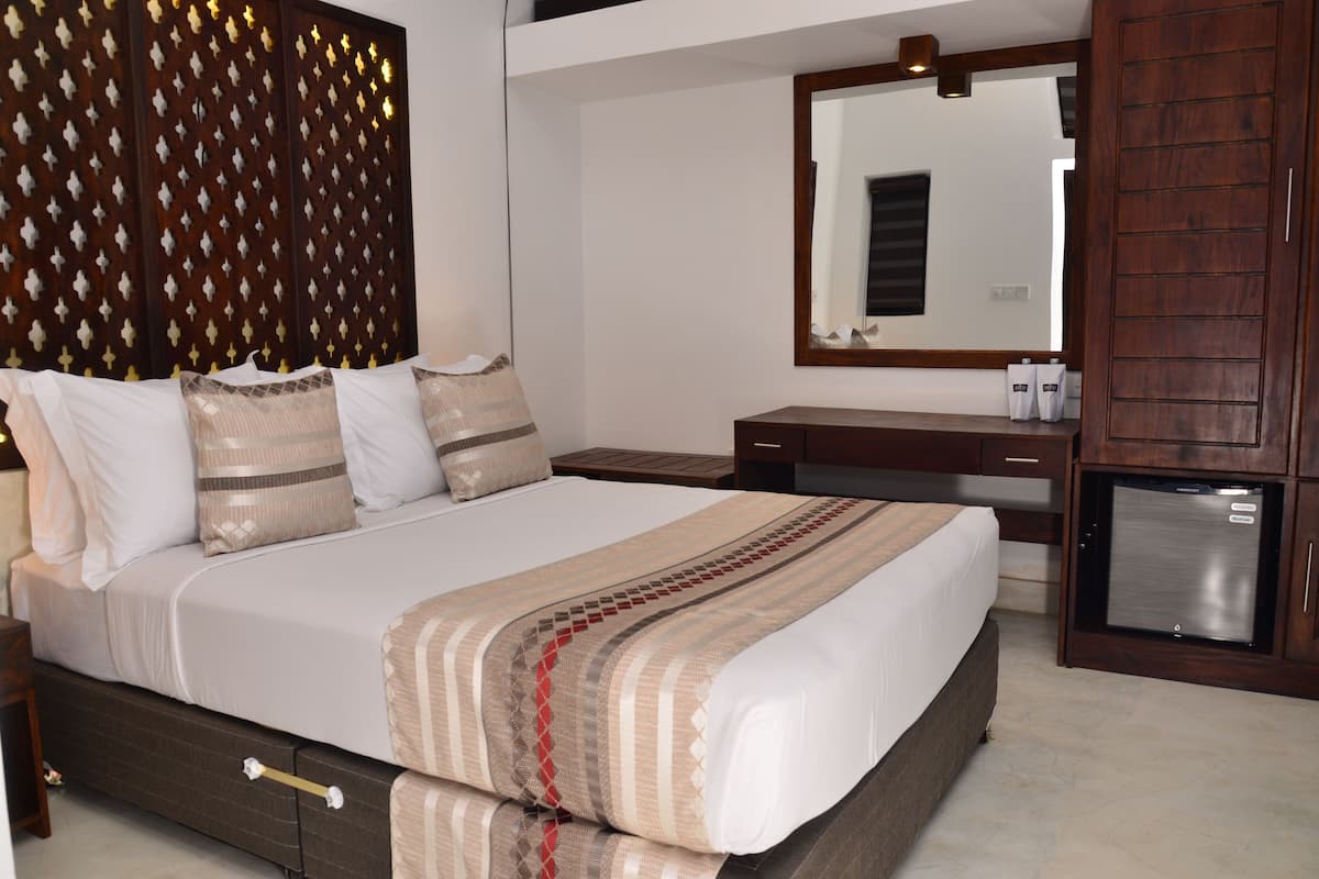 A bedroom with a large bed, a wooden headboard, a dresser, a mirror, and a minibar.