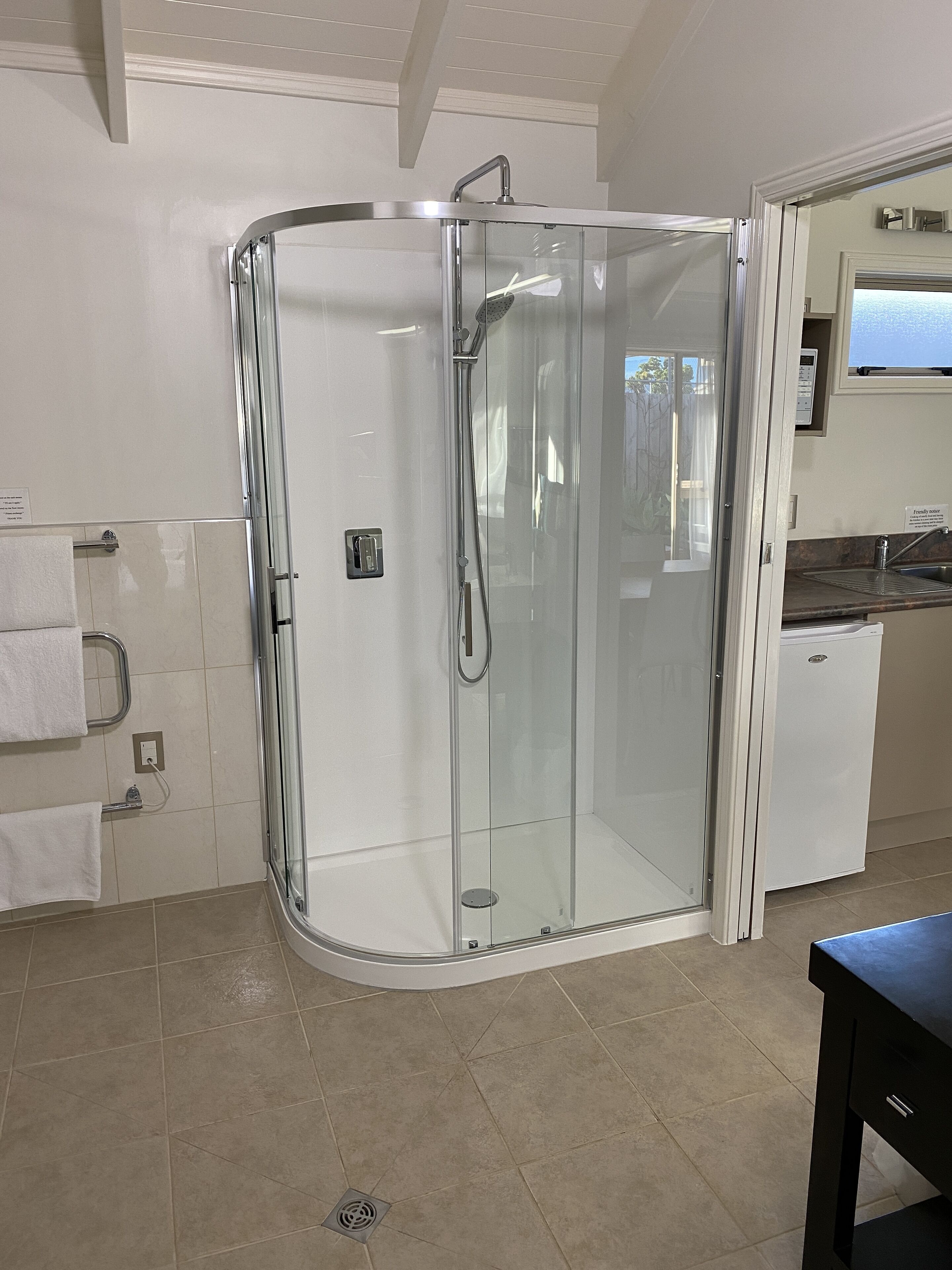 Een moderne badkamer met een douchecabine van glas, een klein wastafeltje en een toilet.