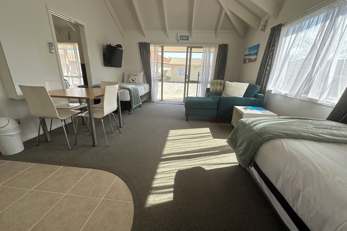 A room with a bed, a desk, chairs, a sofa, and a view of the outside.