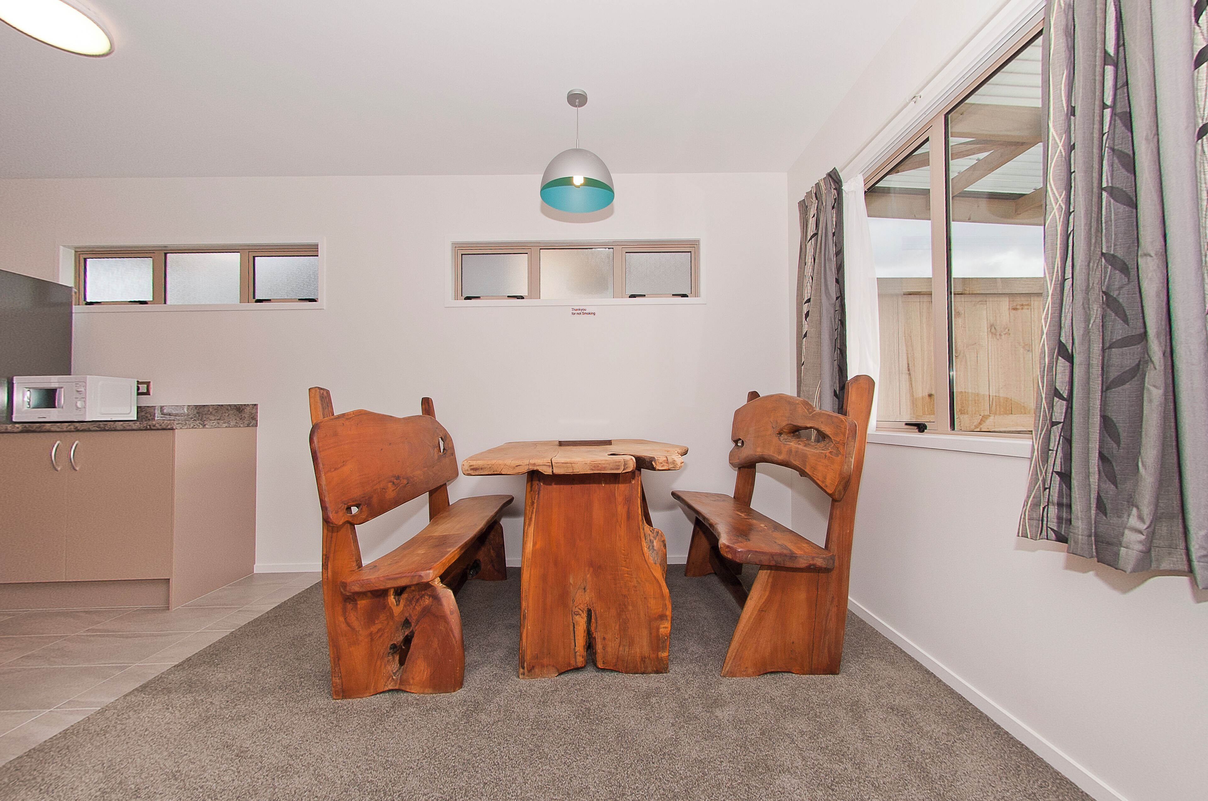 A dining area with a wooden table and benches, a ceiling light, a microwave, and a window with curtains.