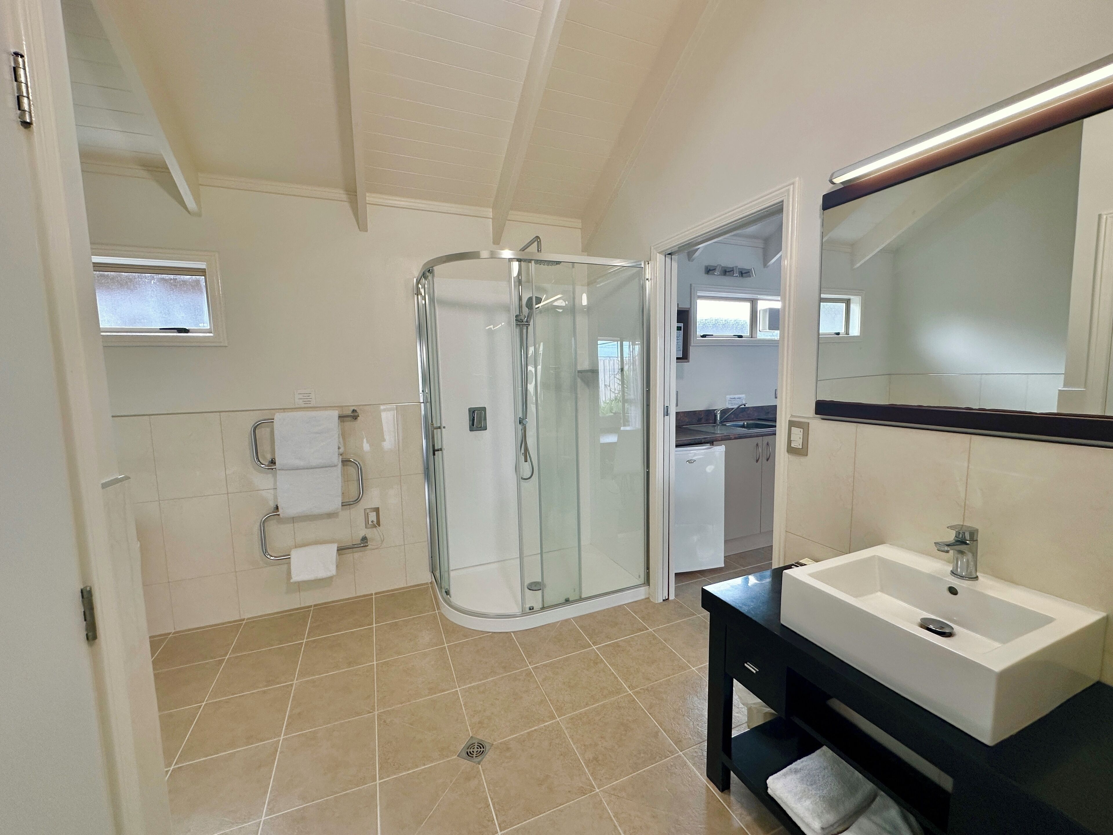 A modern bathroom with a glass-enclosed shower, a sink with a mirror, and a window above the sink.