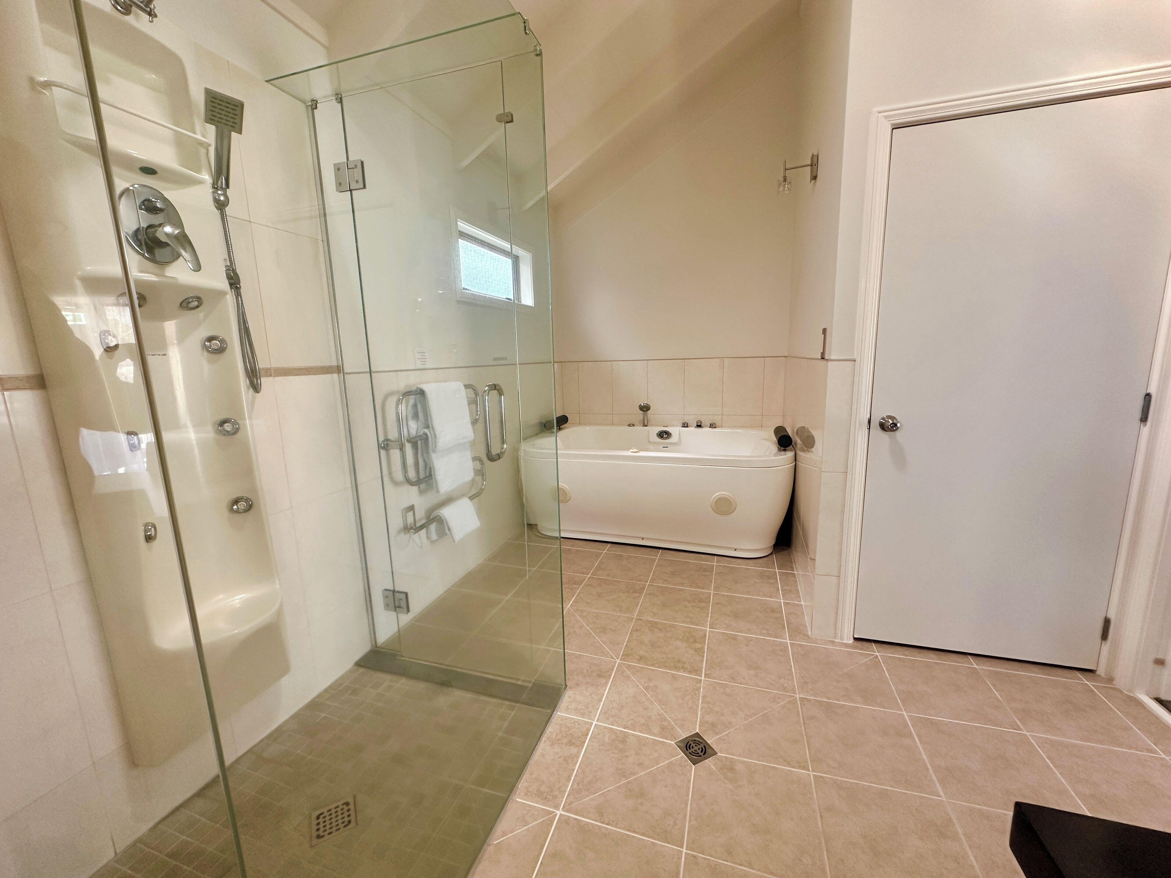 A modern bathroom with a glass-enclosed shower, a white bathtub, and a door.