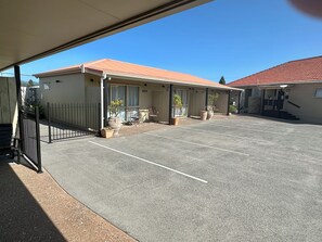 A motel with a covered parking area, outdoor seating, and potted plants. - The Olive Motel (Coromandel)