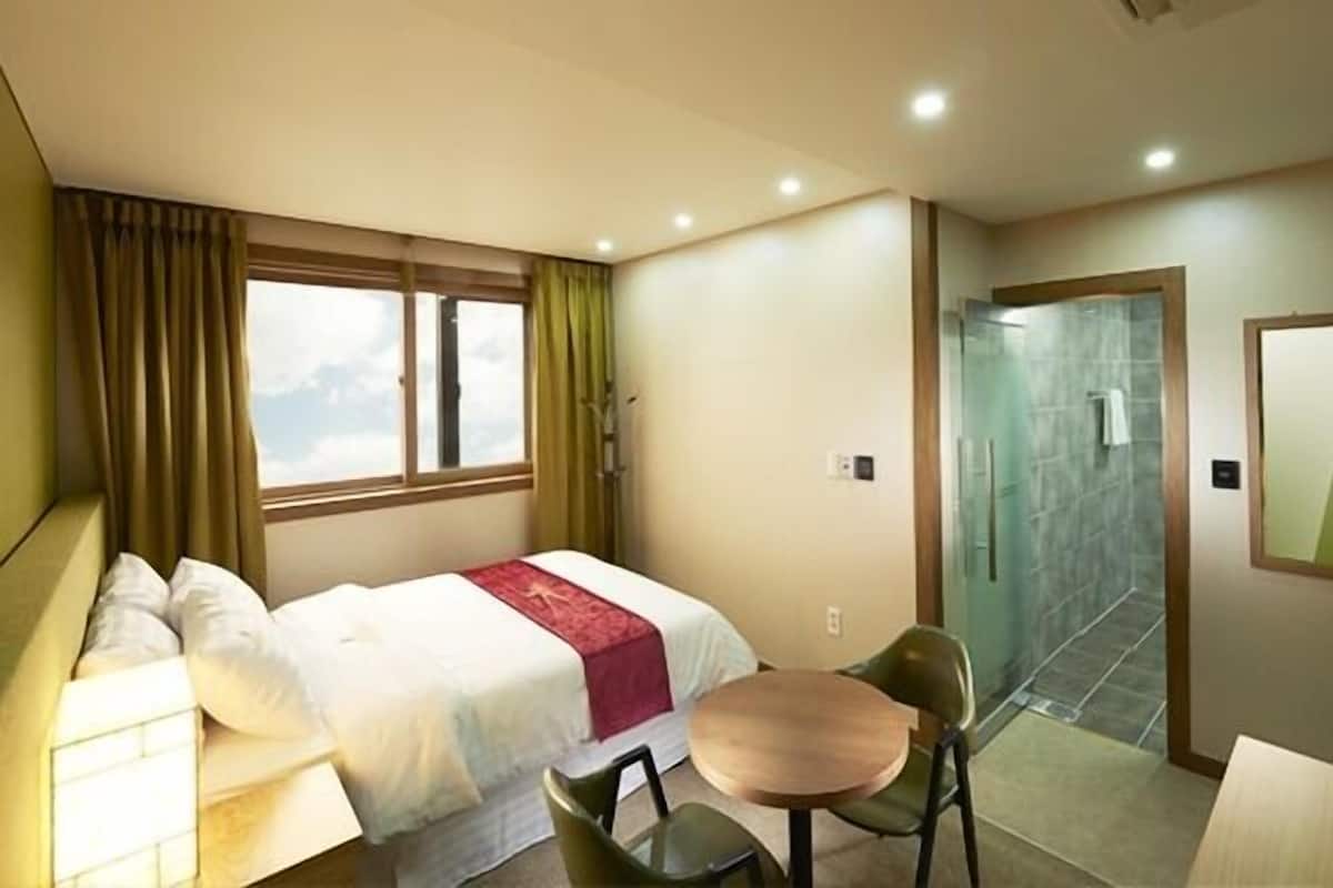 Ein Hotelzimmer mit einem Bett, einem kleinen Tisch, einem Sessel, einer Couch und einem Duschbereich.