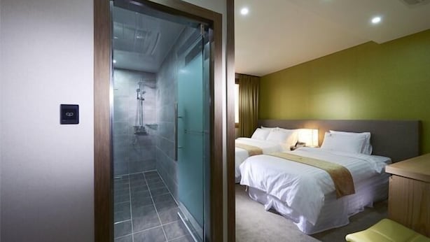 A hotel room with a glass door leading to a shower area, a bed with a headboard, and a bedside table with a lamp. - Benikea Central Hotel (Tongyeong)
