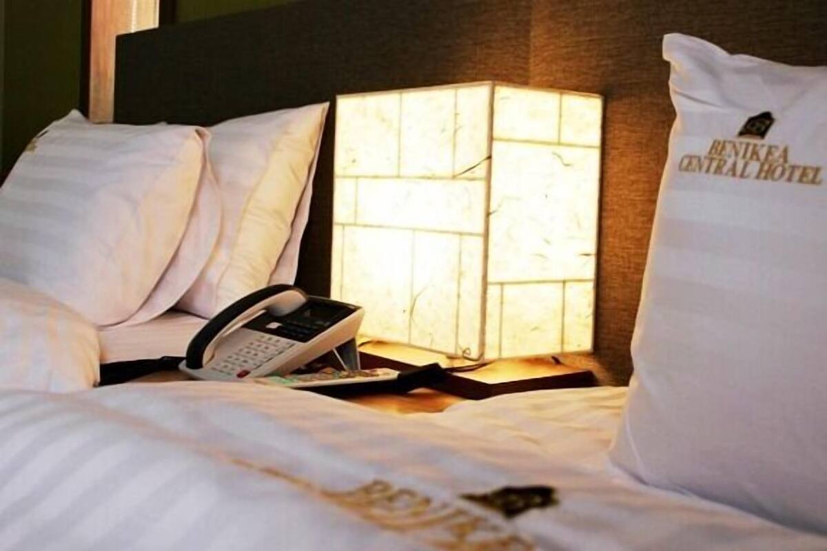Ein Hotelzimmer mit Bett, Nachttischlampe, Telefon und Kopfkissen mit dem Namen des Hotels.