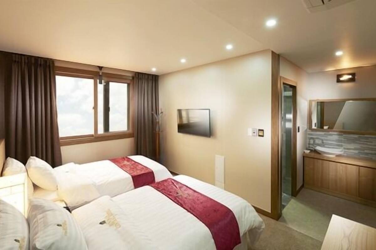 Ein Hotelzimmer mit zwei Betten, einem Fernseher, einem Spiegel und einem Badezimmer mit Dusche.