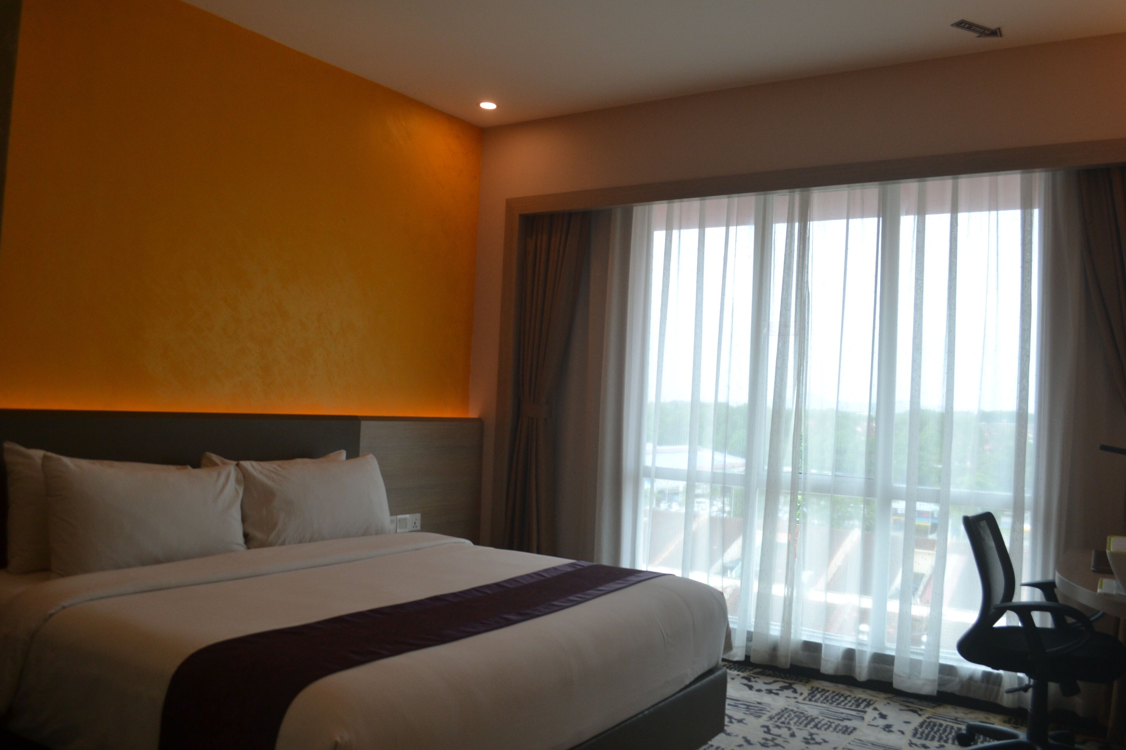 A hotel room with a large bed, a headboard, a window with curtains, and a chair.