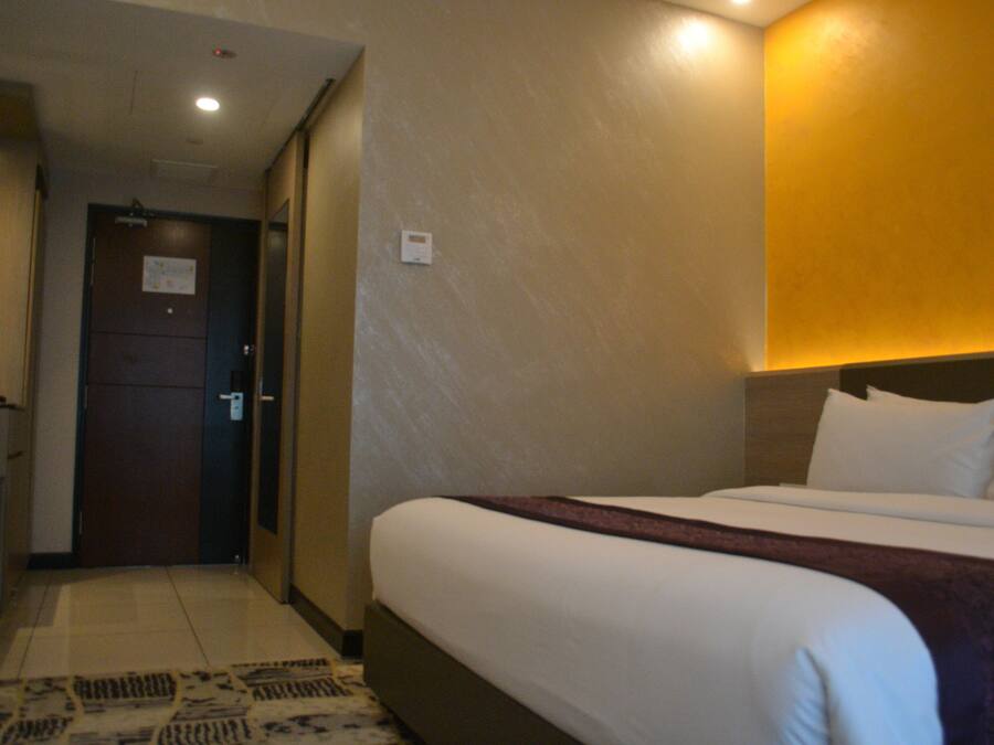 A hotel room with a bed, a desk, and a door.