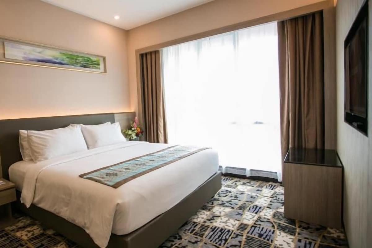 A hotel room with a bed, a nightstand, a TV, and a window with curtains.