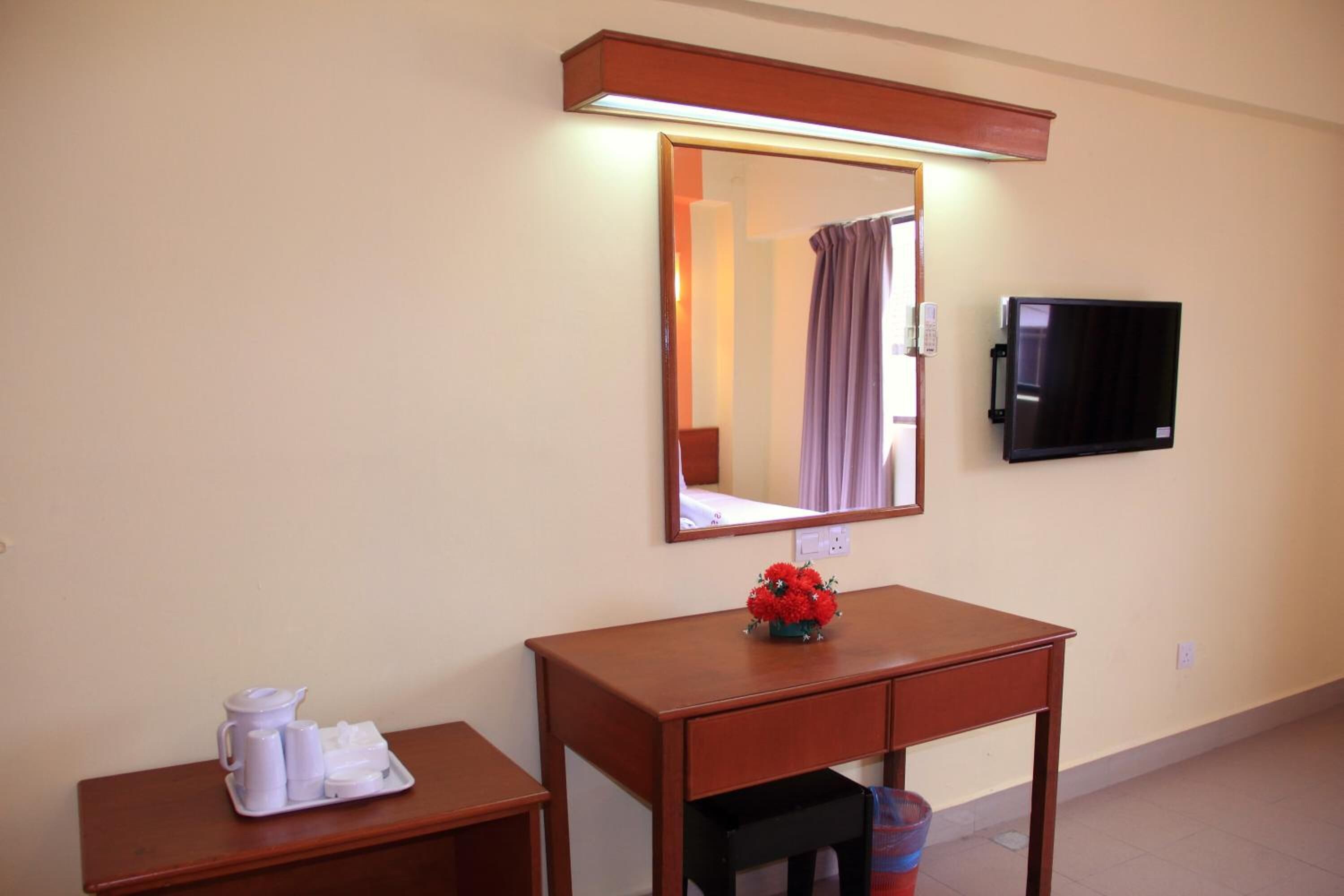 A hotel room with a wooden desk, a mirror, a television, and a small table with toiletries.