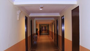 Un pasillo largo y estrecho en un hotel, con puertas a ambos lados, suelo de baldosas e iluminación empotrada en el techo.