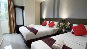 Habitación de hotel con dos camas, cada una con sábanas blancas y almohadas rojas, un ventanal con cortinas y un televisor instalado en la pared.