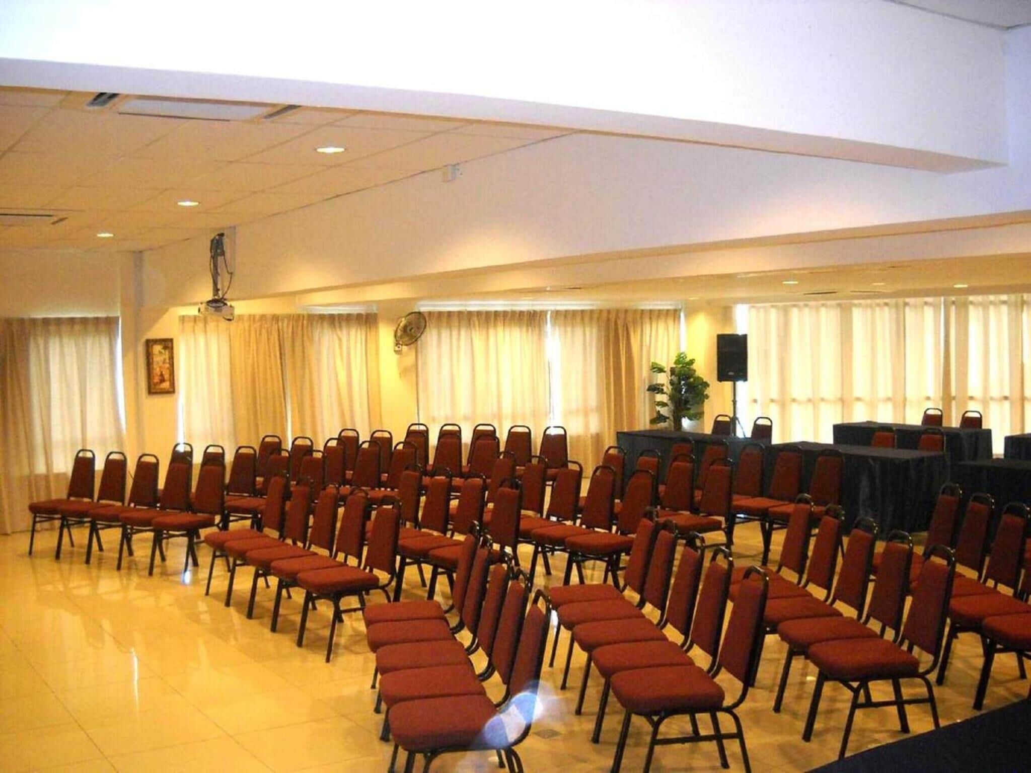 Un salón de conferencias con filas de sillas y un escenario con un atril.