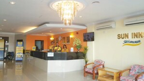 Zona de recepción de un hotel con mostrador, tres empleados, una araña y un letrero en la pared que dice Sun Inns.