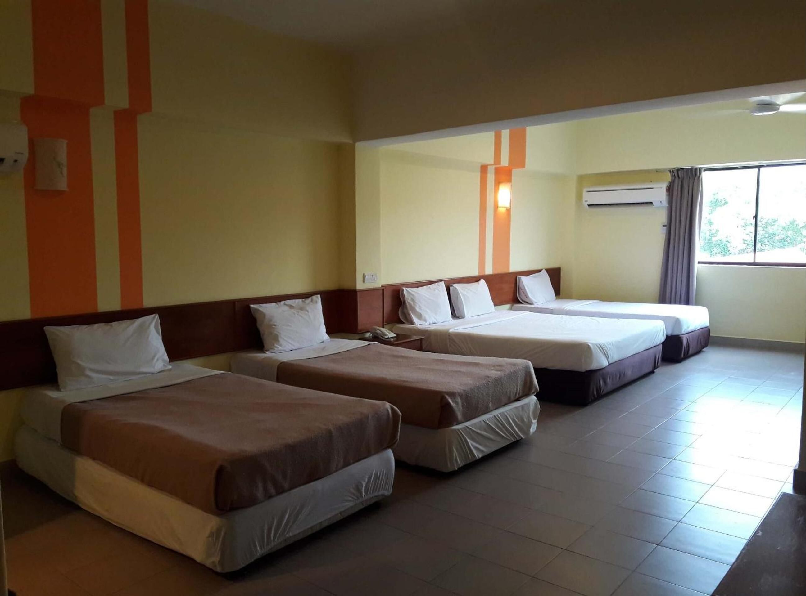 Habitació d'hotel amb quatre llits individuals, un telèfon i una finestra amb cortines.