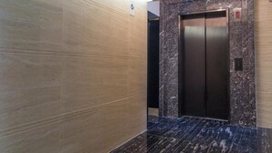 Um elevador moderno com acabamento em mármore, uma luminária no teto e uma placa indicando o sentido do elevador.