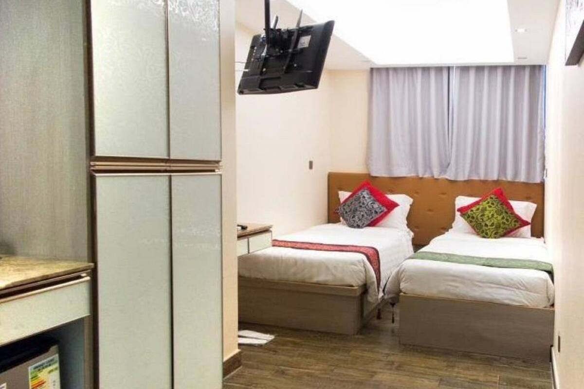 Ett hotellrum med två sängar, en tv som är monterad på väggen och ett fönster med gardiner.