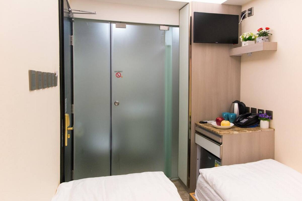 Ett hotellrum med en stängd dörr, en platt-TV som hänger ovanför en träinredd receptionsdisk och ett litet bord med en telefon, en fruktskål och en vattenkokare.