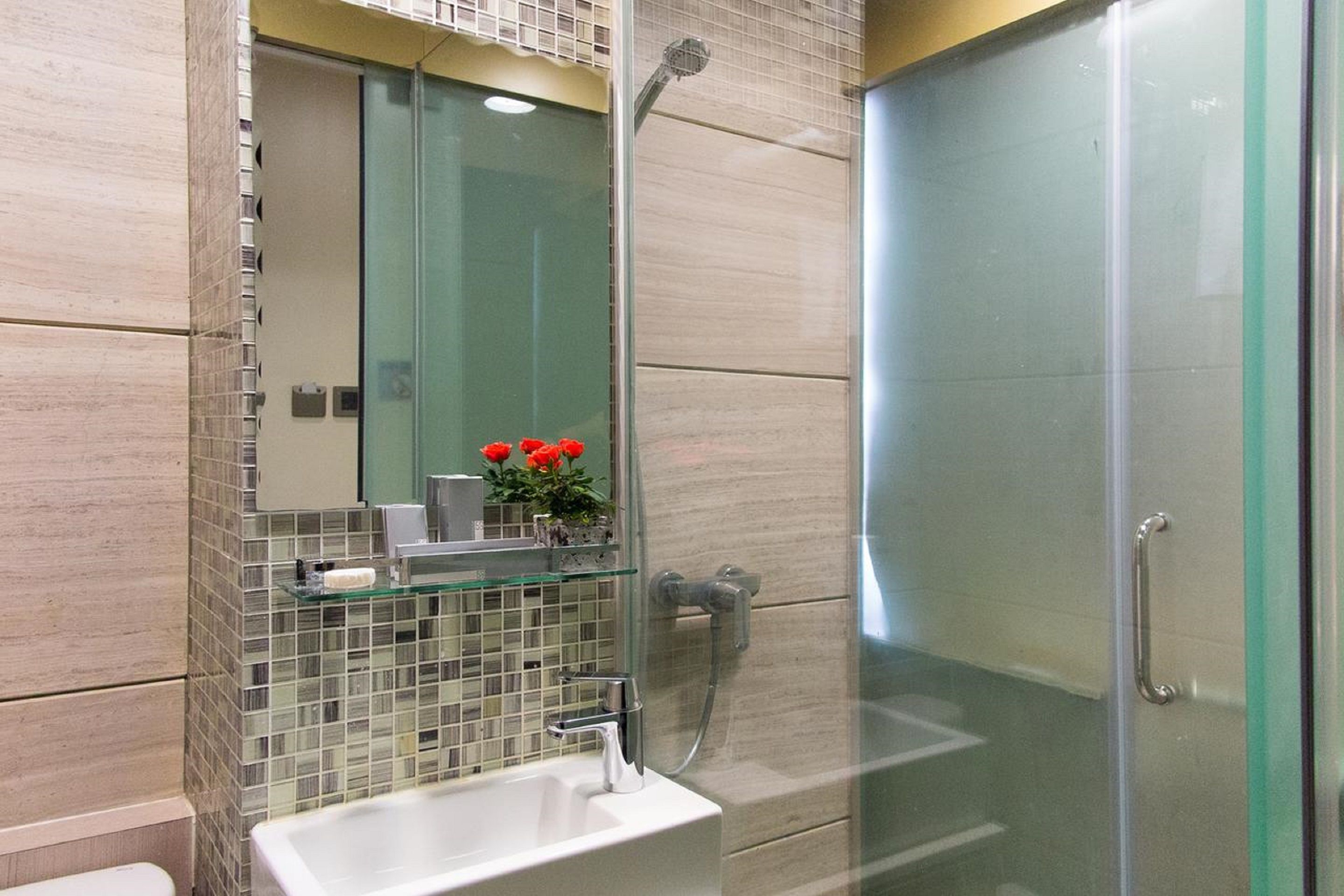A modern bathroom with a glass shower enclosure, a glass-topped sink, and a mirror above the sink.