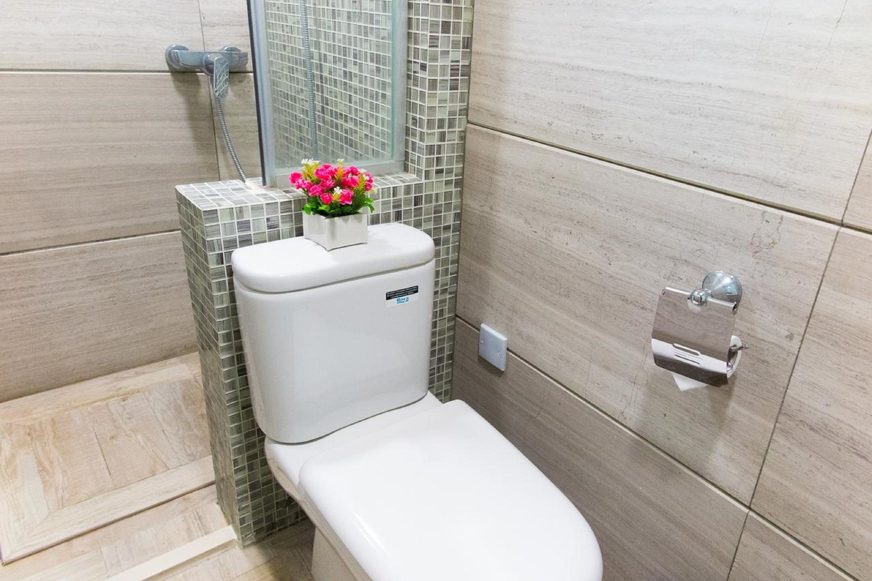 A modern bathroom with a toilet, a shower, and a small flower arrangement on the wall.