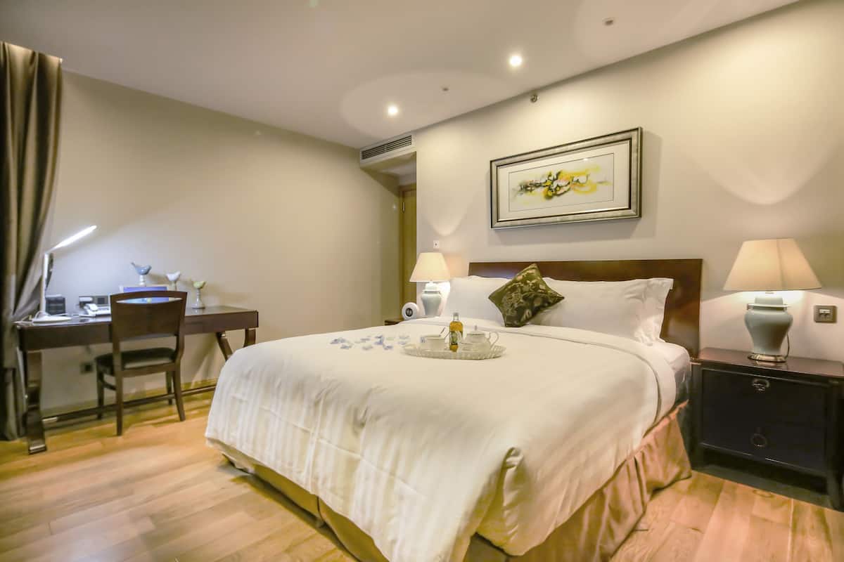 A hotel room with a bed, bedside lamps, a desk, and a chair.