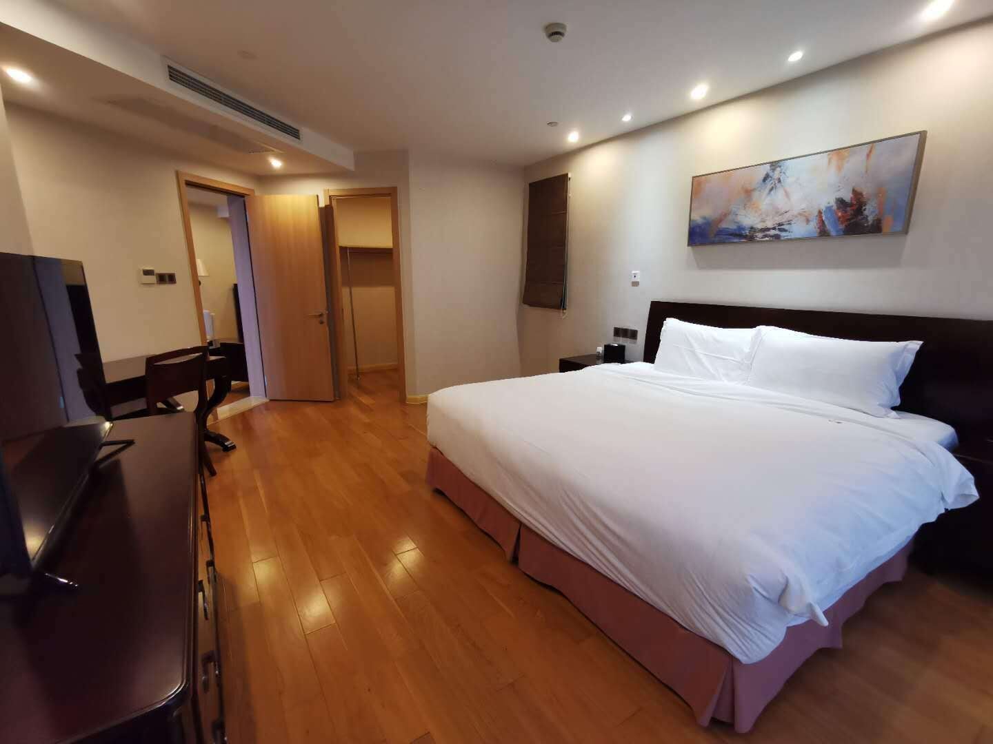 Habitación de hotel con una cama grande, un escritorio y una silla. Hay un cuadro en la pared y una puerta que da a otra habitación.