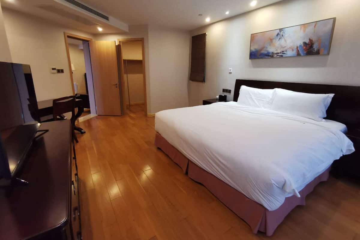 A hotel room with a large bed, a desk, and a chair. There is a painting on the wall and a door leading to another room.