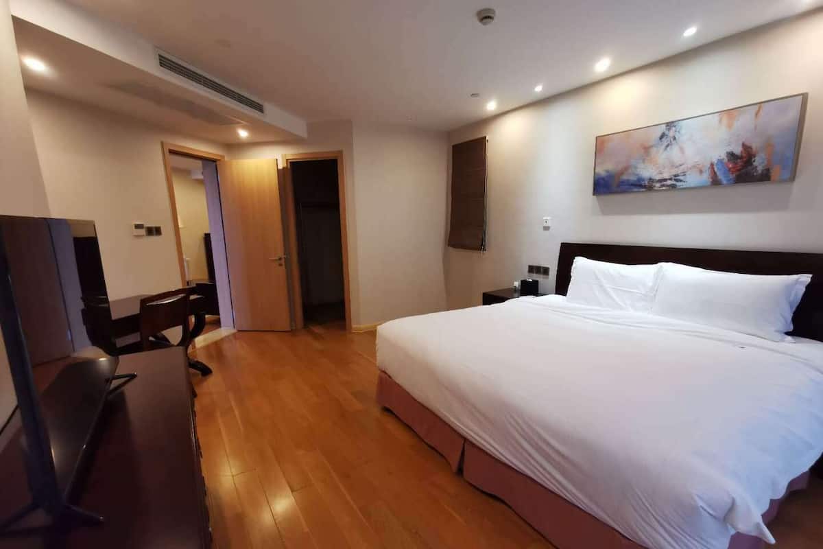 A hotel room with a large bed, a desk with a chair, a wardrobe, and a painting on the wall.