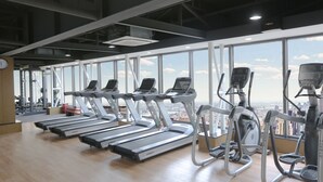 A gym with treadmills and elliptical machines, large windows with a city view, and a wooden floor. - Green Court Residence Jinqiao Diamond Shanghai (Shanghai)