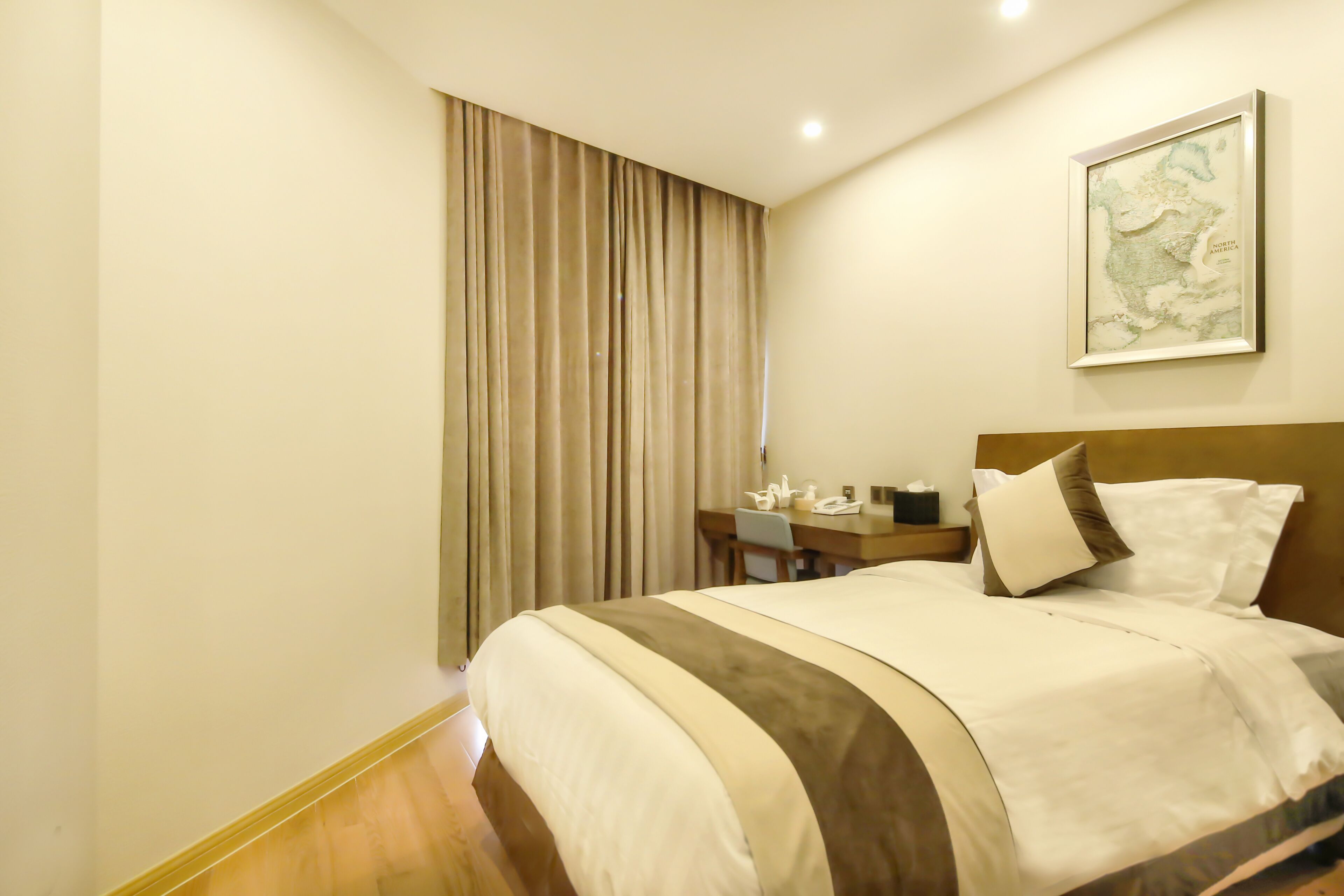 A hotel room with a large bed, a desk with a chair, a map on the wall, and a curtain on the window.