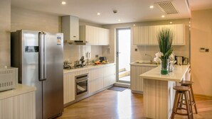A modern kitchen with stainless steel appliances, light wood cabinetry, and a central island with stools. - Green Court Residence Jinqiao Diamond Shanghai (Shanghai)
