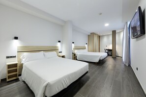Ein Hotelzimmer mit zwei Betten, einem Schreibtisch und einem an der Wand befestigten Fernseher.