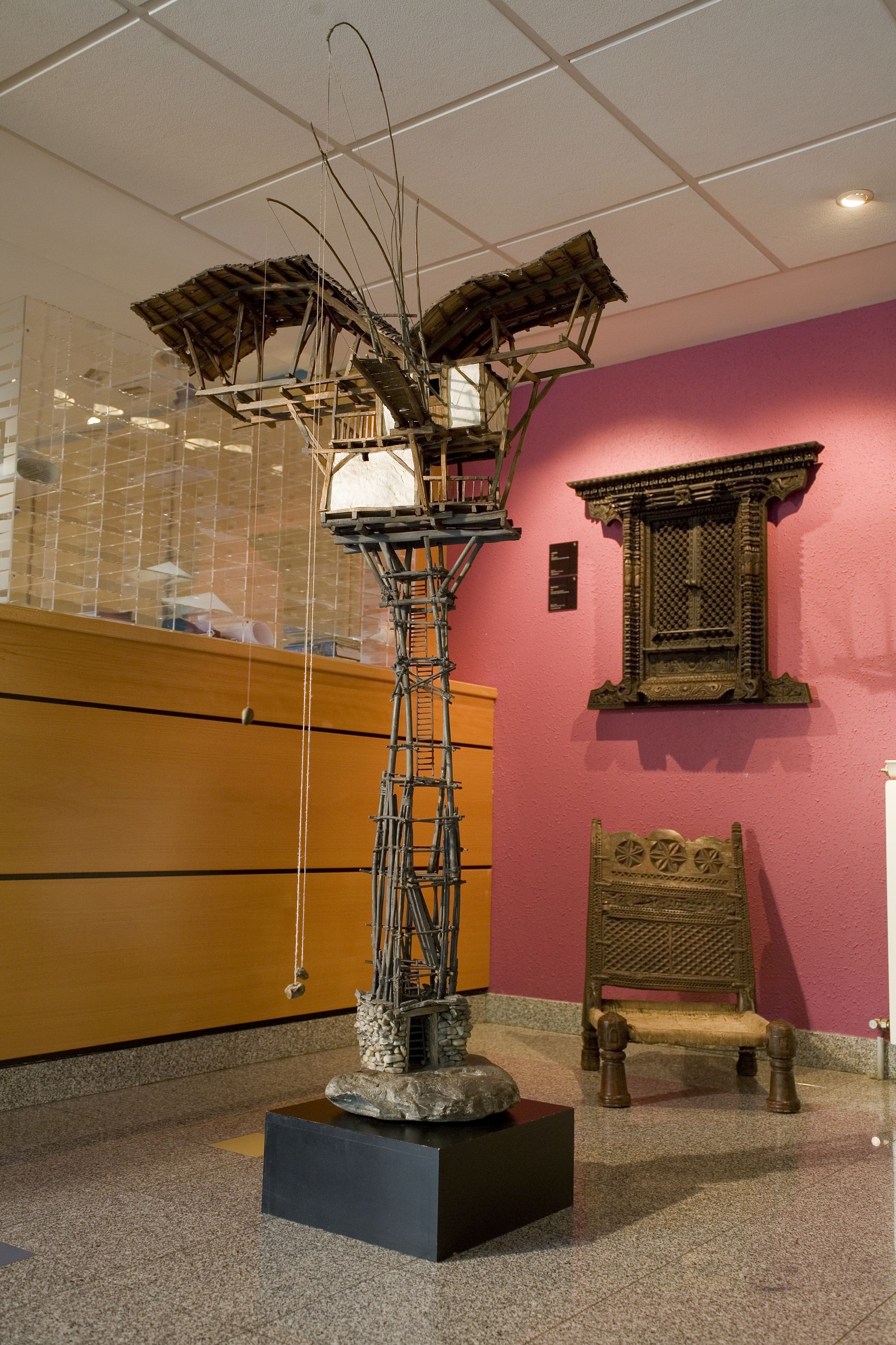 Una habitación con una escultura única sobre un pedestal, un armario de madera y una silla tradicional.