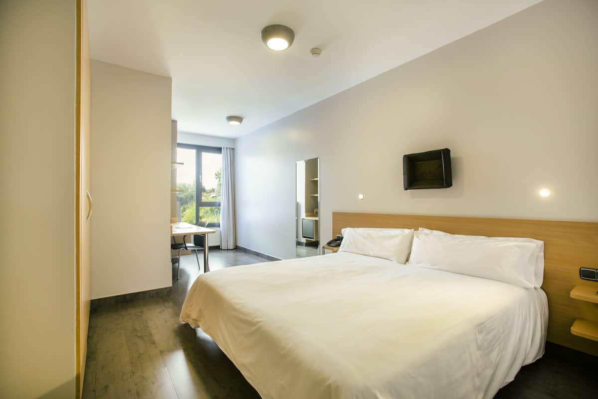 A modern hotel room with a large bed, a desk, and a chair.