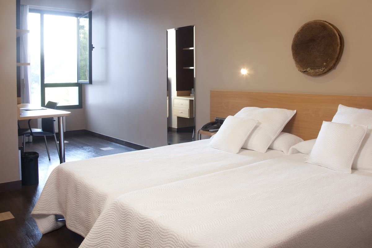 A hotel room with two beds, a desk, and a chair.