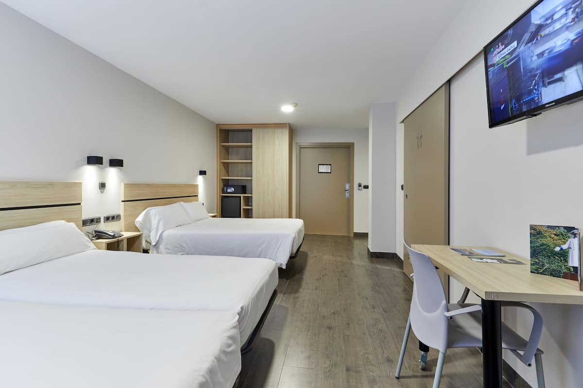 A hotel room with two beds, a desk, a TV, and a bookshelf.