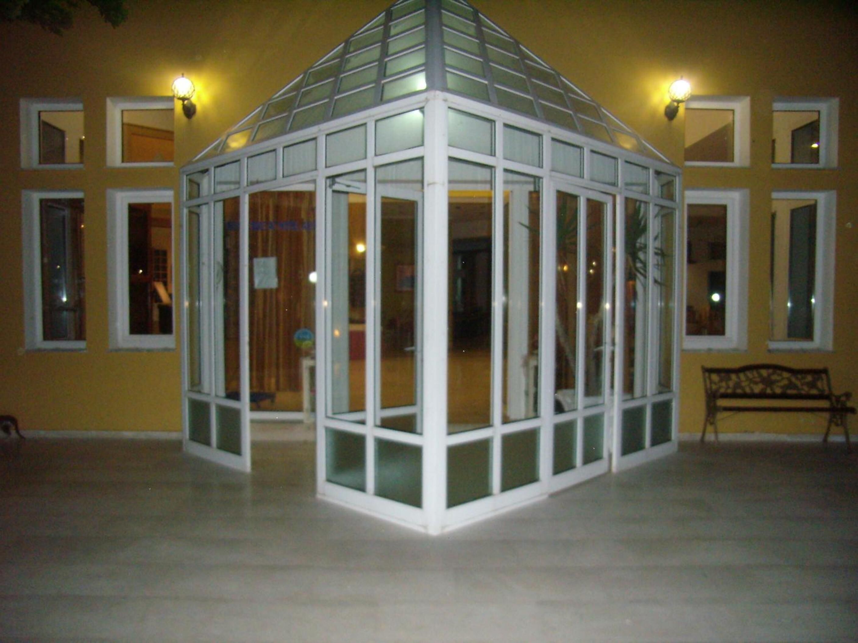 Ein gläsernes, weißes Gazebo vor einer gelben Wand mit mehreren Fenstern.